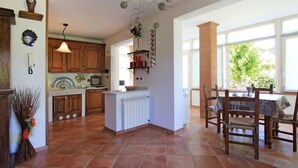 Une cuisine spacieuse avec des meubles en bois, un îlot central et un coin repas agrémenté d’un pilier en briques et de grandes fenêtres.