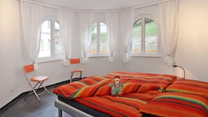 Een slaapkamer met een bed, twee stoelen en drie ramen voorzien van gordijnen.