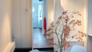 En modern inredning med ett vitt matbord och stolar, en vas med torkade blommor och en hall som leder till ett annat rum.