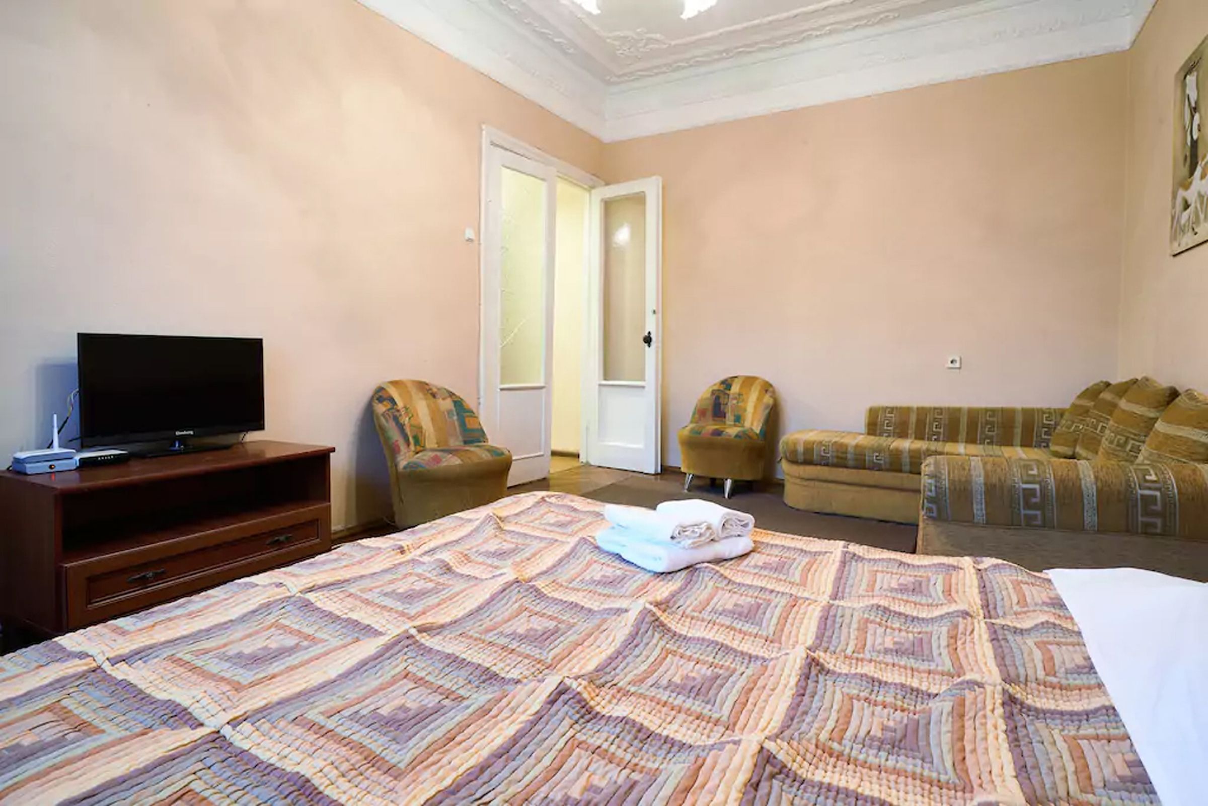 A hotel room with a bed, a television, two armchairs, and a sofa.