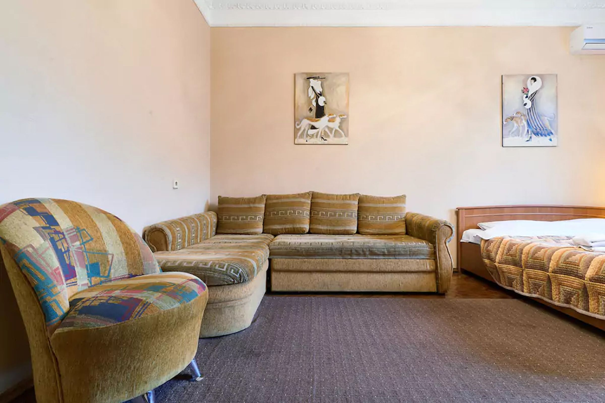 A room with a sofa, a patterned armchair, and a bed. There are two wall-mounted artworks.