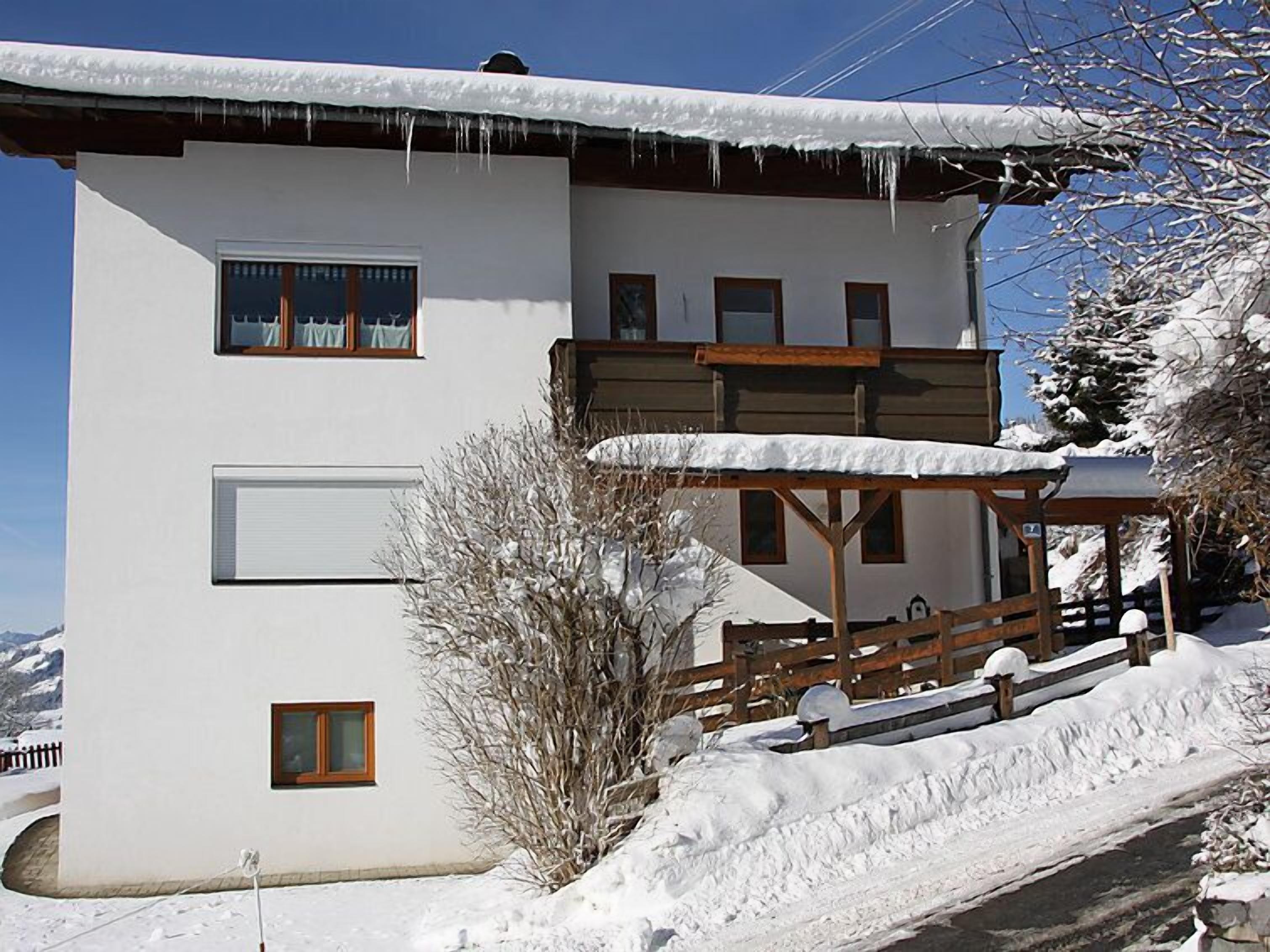 A two-story building with a white exterior, wooden balconies, and a snow-covered roof.