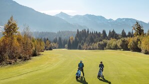 A golf course with two players and their bags, surrounded by trees and mountains. - Apartment Straif by Interhome (Kirchberg in Tirol)