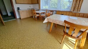 A dining area with a table and chairs, a kitchen with wooden cabinets, and a window with curtains. - Apartment Straif by Interhome (Kirchberg in Tirol)