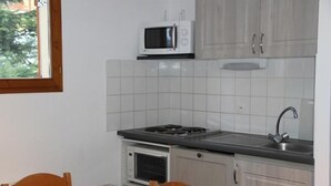 A compact kitchen with a microwave, stove, oven, and sink. There is a table with chairs and a window with a view of trees. - 300m from ski slopes, floor -1, view mountain, parking, tv, ski locker, 36m², Valfréjus (Valfréjus)