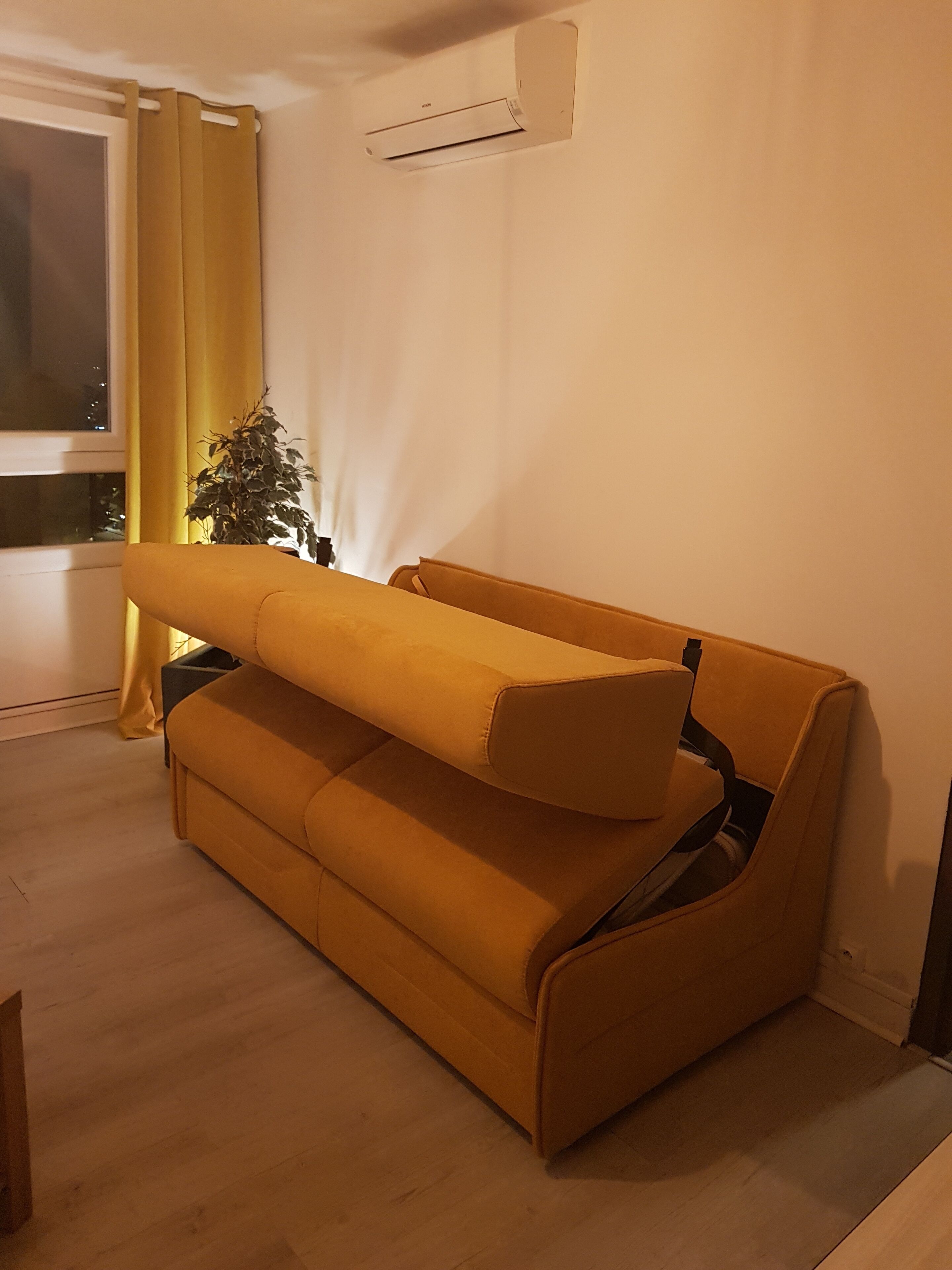 Um quarto com um sofá, uma planta em vaso e uma janela com cortinas.