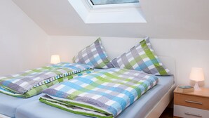 A bedroom with a skylight, a bed with a checkered bedspread, two pillows, a bedside table with a lamp, and a nightstand with a book.