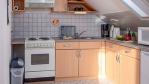 A compact kitchen with a stove, sink, and microwave. It includes wooden cabinets, a tiled backsplash, and a window above the sink.