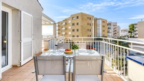 Ein Balkon mit Glastisch und Stühlen, einem Blumentopf und Blick auf benachbarte Gebäude.