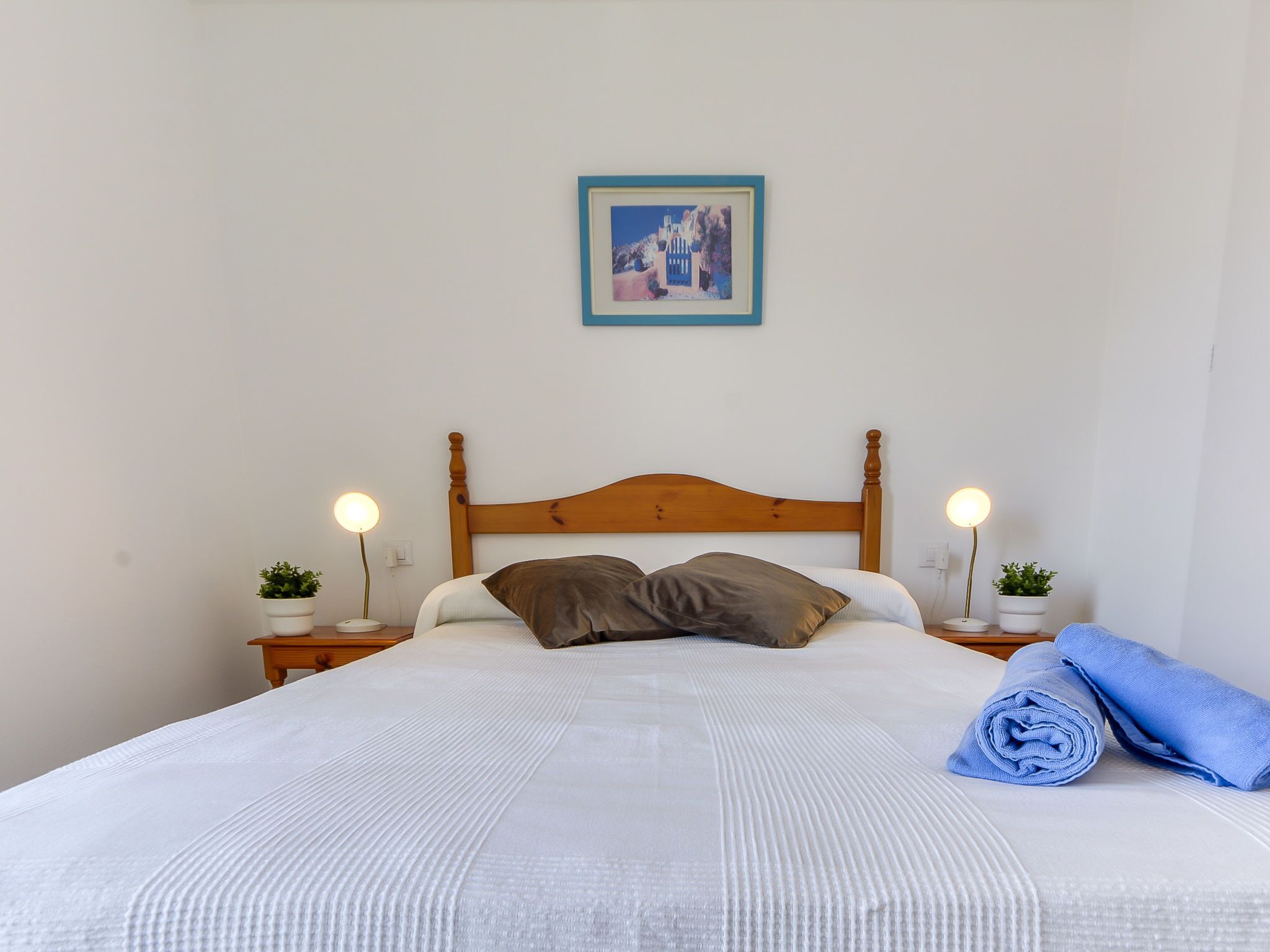 A neatly made bed with a wooden headboard, two bedside tables with lamps, and a framed picture on the wall.