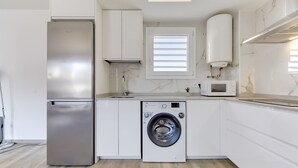 Eine moderne Küche mit Kühlschrank aus Edelstahl, einer integrierten Waschmaschine, einer Mikrowelle und einem Fenster mit Jalousien.