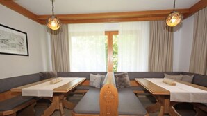 Un comedor con bancos y mesas de madera, dos lámparas colgantes y vistas al exterior con vegetación.