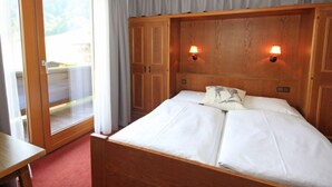 Un dormitorio con cabecera de madera, dos lámparas de noche, una cama con ropa de cama blanca, un ventanal corredero y una alfombra roja.