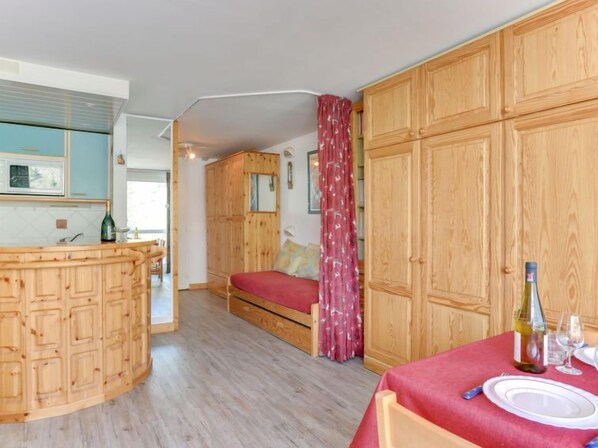 A compact room with a wooden cabinet, a bed with a red bedspread, and a dining area with a table set for two.