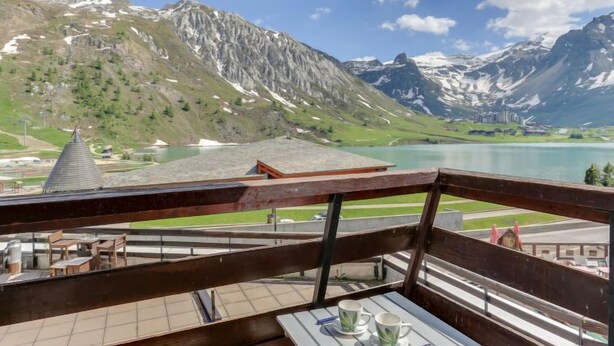 Een balkon met een tafel en stoelen met uitzicht op een bergmeer en een dorp.