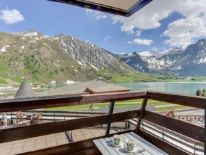 A balcony with a table and chairs overlooking a mountain lake and a village.