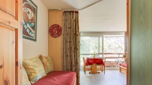 Een kamer met een rode bank, een eettafel met stoelen en een groot raam.
