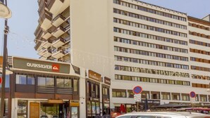 Een gebouw met een Quiksilver bord op de begane grond, meerdere verdiepingen met balkons, en een parkeerplaats met een witte auto.