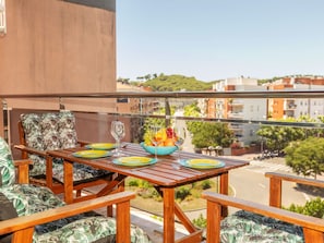 A balcony with a wooden table set for two, a bowl of fruit, and two wine glasses.