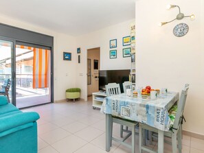 En moderne stue med sofa, spisebord med dug, fjernsyn og en lille grøn skammel.