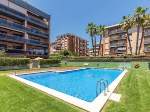 A swimming pool surrounded by well-maintained grass, with multi-story residential buildings in the background.
