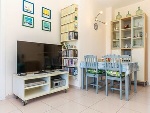 En stue med et fladskærms-tv, en bogreol, et spisebord med stole og et skab med glas.
