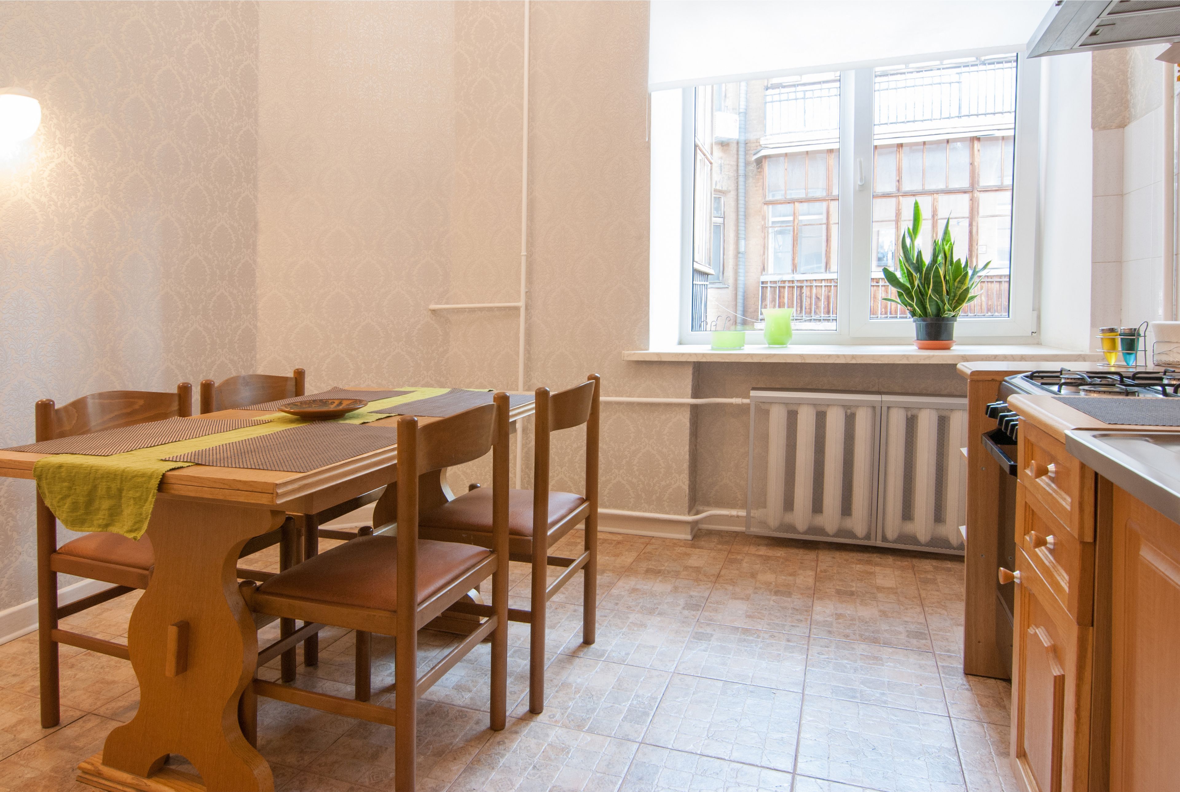 Una cocina con una mesa de comedor, sillas, una ventana con plantas y un radiador.