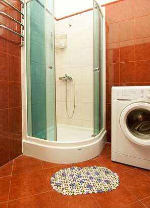 Eine Dusche mit Glastür, eine Waschmaschine und ein gemustertes Teppich