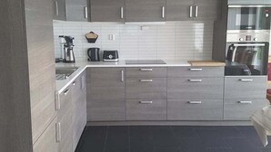 A modern kitchen with grey cabinets, a black countertop, and a built-in oven. - Lyngsalpan Cruise Lodge (Lyngen)