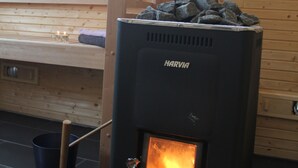 A Harvia wood stove with a fire burning inside, placed in a room with wooden walls and a window. - Lyngsalpan Cruise Lodge (Lyngen)