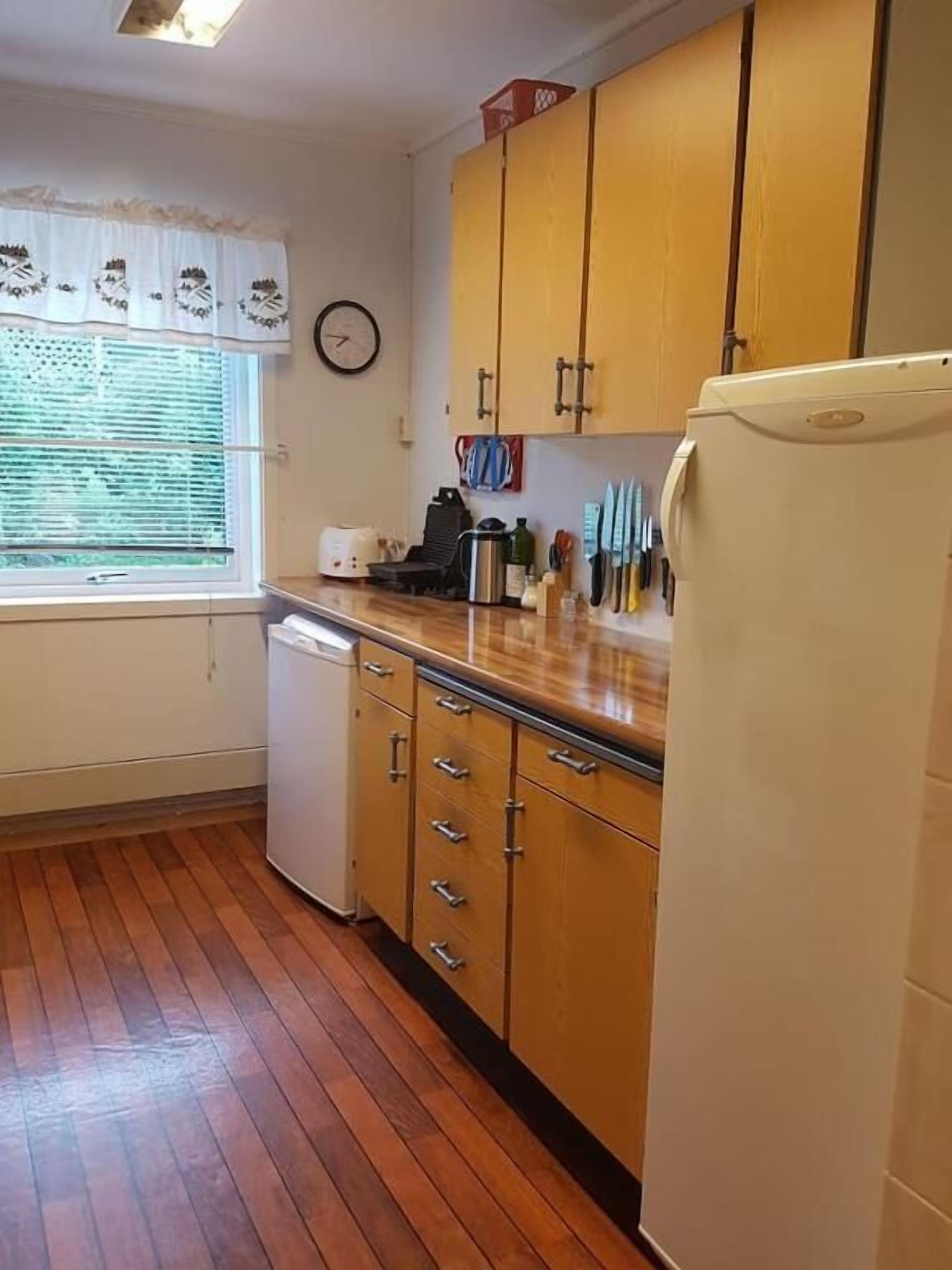Una cocina compacta con armarios de madera, un refrigerador blanco y un ventanal con persianas.