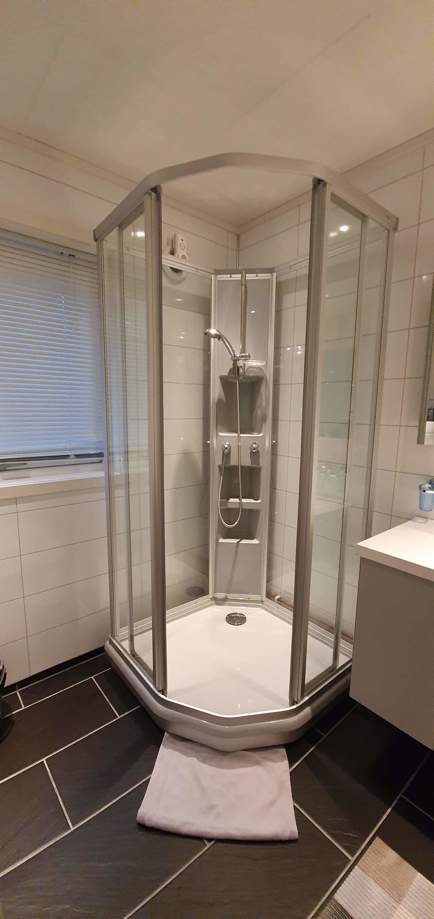 Eine Eckdusche mit Glastrennwand, ein weißes Waschbecken und ein Handtuch auf dem Boden.