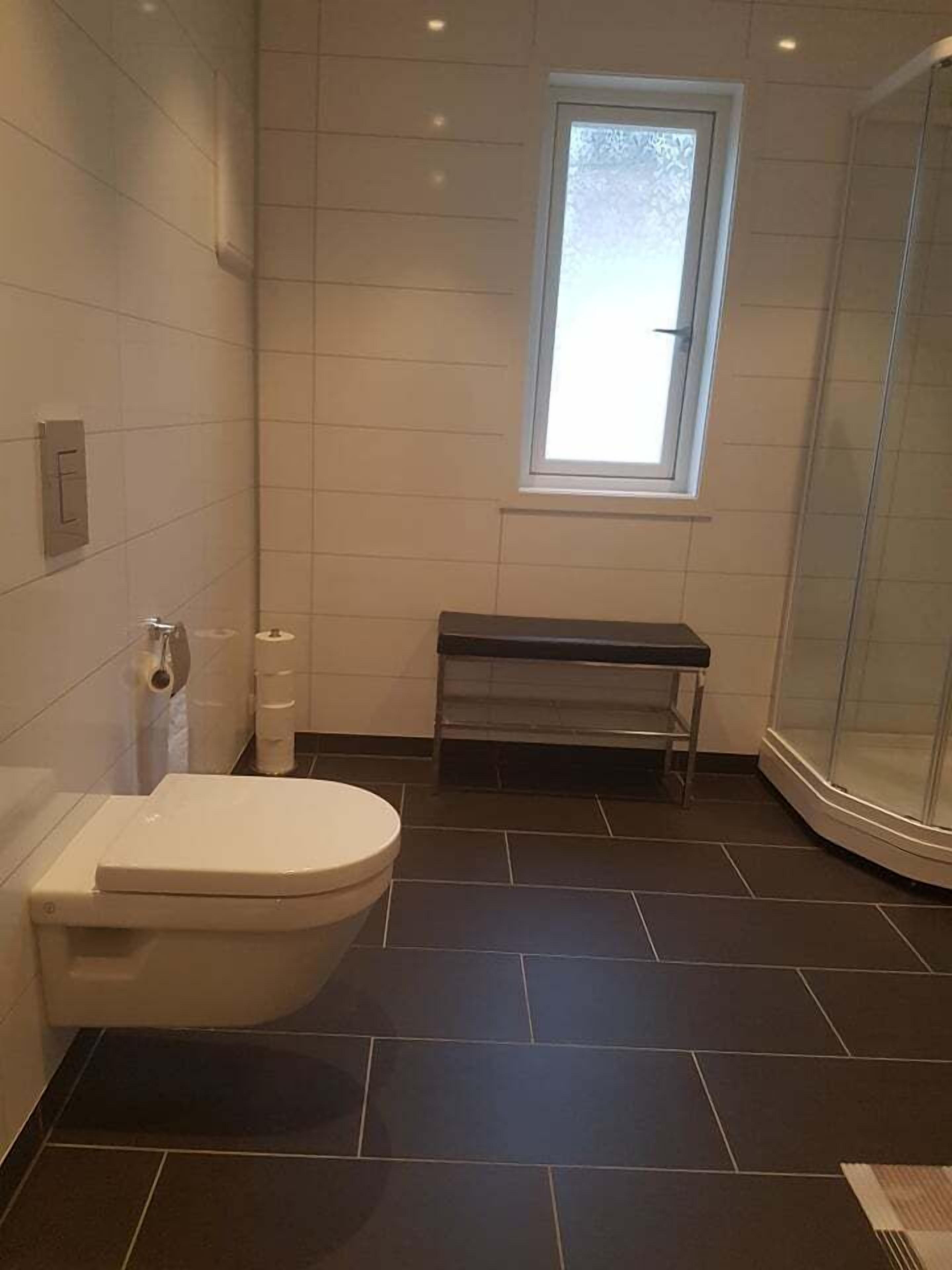 A bathroom with a toilet, a bench, and a shower area.