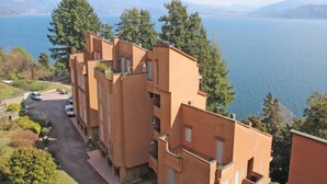 A multi-story building with balconies overlooking a lake, surrounded by greenery.