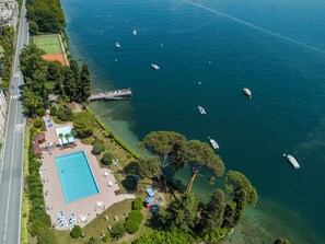 Ett flygbildsfoto av en fastighet vid kusten med en swimmingpool, solstolar och båtar i vattnet.