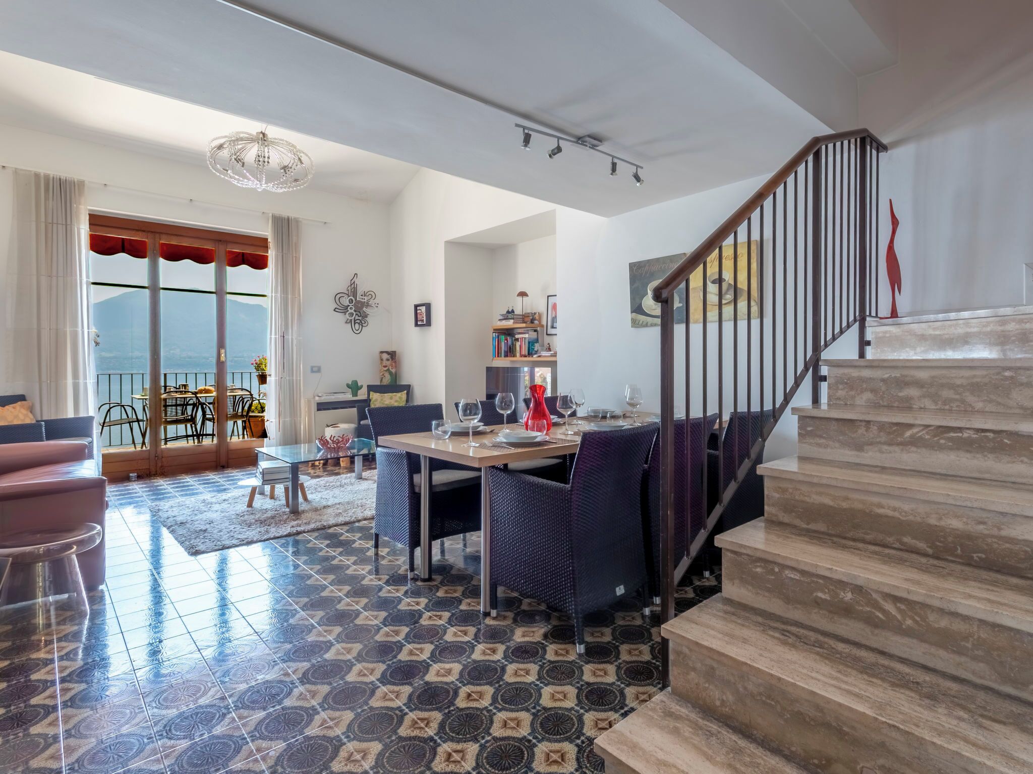 A spacious living area with a dining table, chairs, a staircase, and a view of the outdoors.