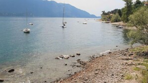 A calm lake with several sailboats anchored, surrounded by rocky shores and distant mountains.