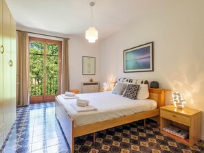 Ein Schlafzimmer mit Bett, Nachttischen, einem Fenster mit Vorhängen, einem gerahmten Bild und einem gemusterten Boden.