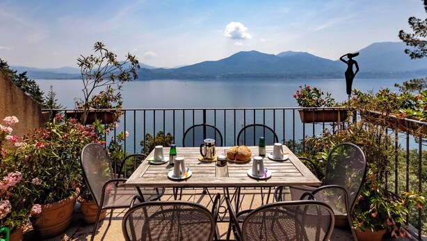 A table set for two with chairs, a view of a lake, mountains, and a statue.