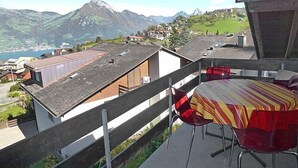 A balcony with a view of a mountain and a lake. There are red and yellow striped chairs and a table. - Flodana by Interhome (Emmetten)