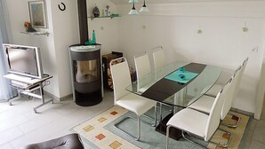 A modern living room with a glass dining table, white chairs, a black fireplace, and a TV on a stand. - Flodana by Interhome (Emmetten)
