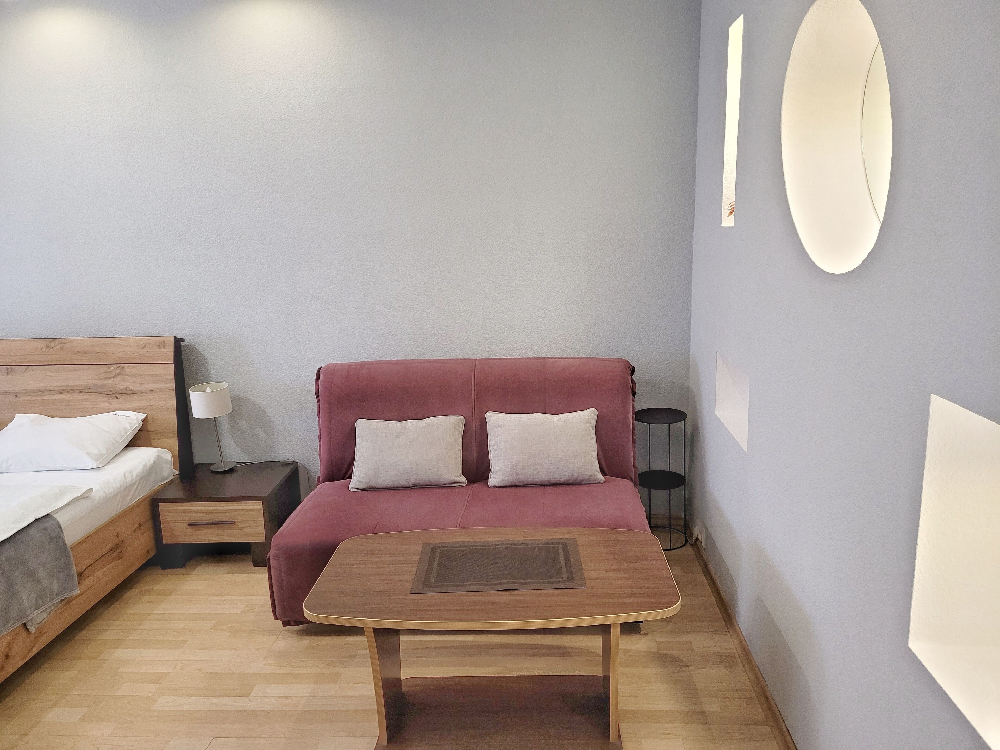 Una habitación de hotel moderna con una cama de madera, un sofá rojo, una mesita y una lámpara.