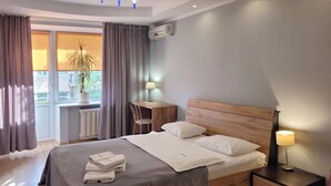 A neatly made bed with pillows and a blanket, a bedside table with a lamp, a window with curtains, and a radiator. - Home-Hotel Malaya Zhitomirskaya 10-1 (Kyiv)
