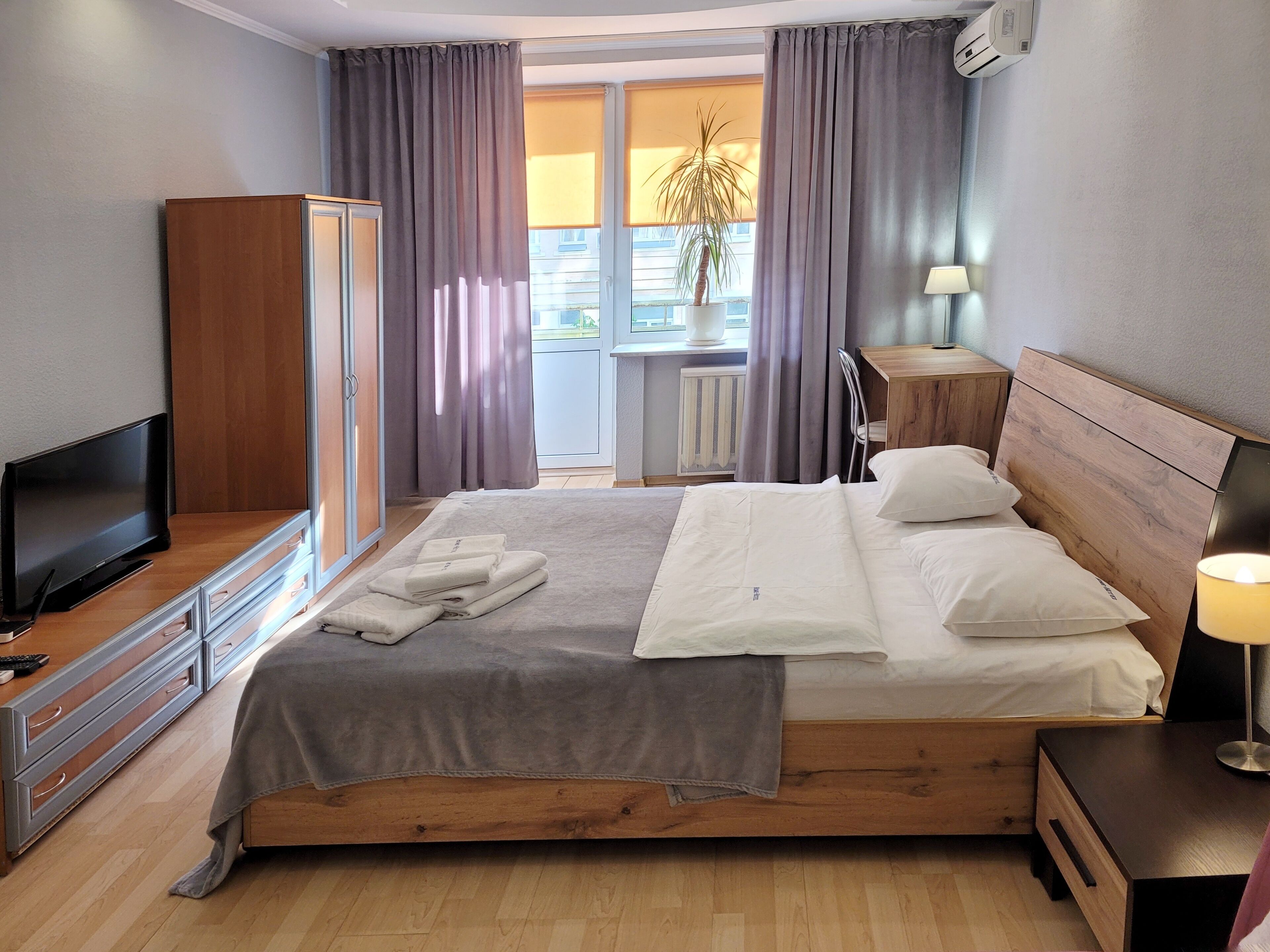 Une chambre d’hôtel bien rangée, avec un lit, une télévision, une armoire et une fenêtre avec des rideaux.