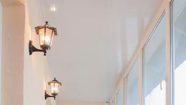Un couloir étroit avec une table et une chaise, deux lampes fixées au mur et une fenêtre avec des stores.