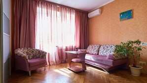 Un salon doté d’un parquet en bois disposé en motif chevron, d’un canapé rose, d’un fauteuil assorti, d’une petite table d’appoint en bois et d’une plante en pot.