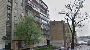 Un immeuble à plusieurs étages, avec une entrée au rez-de-chaussée, des balcons et un arbre devant.