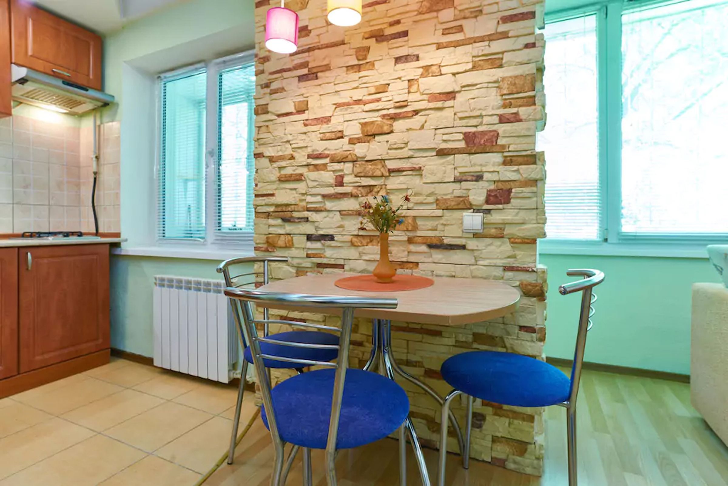 Een keuken met een stenen muur, een ronde tafel met stoelen en een raam met jaloezieën.