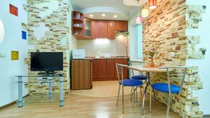 A compact kitchen with wooden cabinets, a built-in oven, and a dining area with blue chairs. - Home-Hotel Metropolita Sheptitskogo 1A (Kyiv)