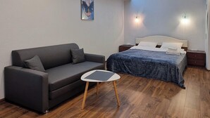 A modern bedroom with a grey sofa, a small white table, a bed with a blue blanket, and a painting on the wall. - Home-Hotel Metropolita Sheptitskogo 1A (Kyiv)